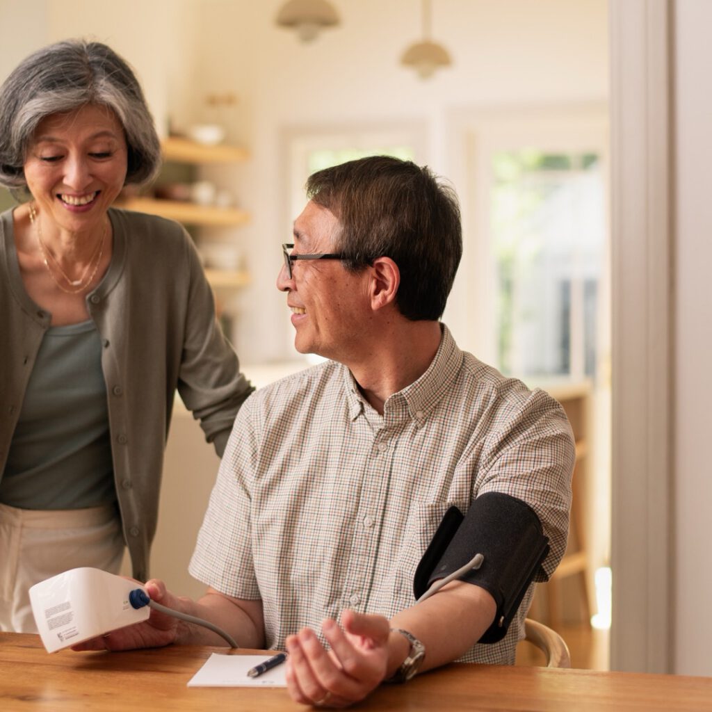 A woman helping a senior man check his blood pressure at home
